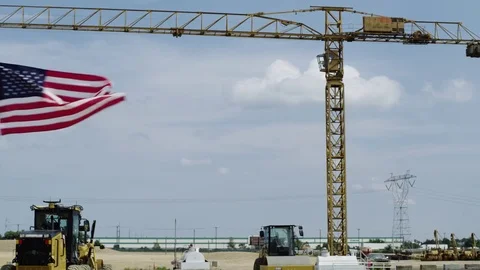 Drone mounted American flag flies in front of construction crame Stock Footage 80133455