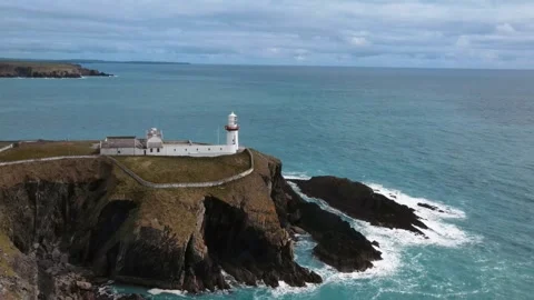 Drone moves away from a white lighthouse over rocks in the ocean, Ireland Stock Footage 267077151