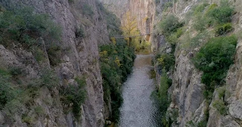 Drone moving along a deep river canyon and in the background a suspension bridge Stock Footage 124387370