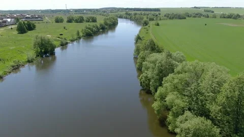 Drone moving forward above calm river and green banks Видео 331829228