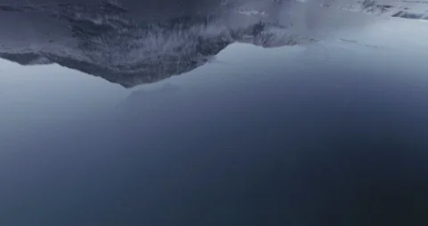 Drone moving forward, reflection of a mountain top in ice covered water Stock Footage 123296358