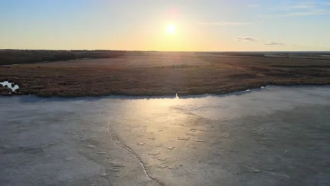 Drone moving slowly forwards towards a setting sun over a frozen pond  Stock Footage 151764248