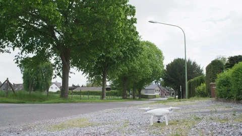 Drone Multicopter taking off into the air on Sidewalk of a Road with green trees 스톡 동영상 118717385