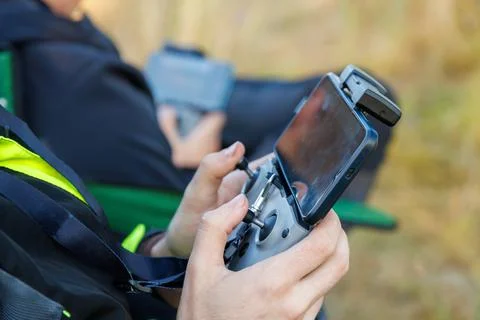 Drone operator hands using remote control with sticks and cellphone as monitor Stock Photos