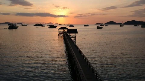 Drone, orange sunset with long jetty, boat and island silhouettes, Komodo In Stock Footage 131437112