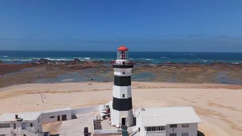 Drone Orbit of Lighthouse with Ocean, Beach, Sand, Blue Sky, and Green Landscape Stock Footage 306255507