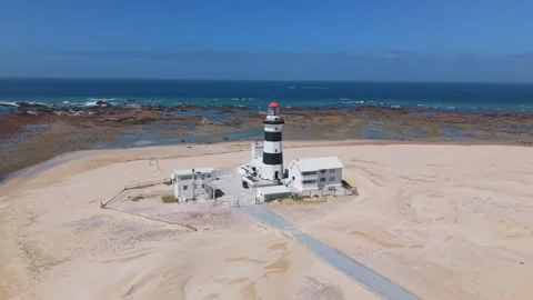 Drone Orbit of Lighthouse with Ocean, Beach, Sand, Blue Sky, and Green Landscape Stock Footage 306263556