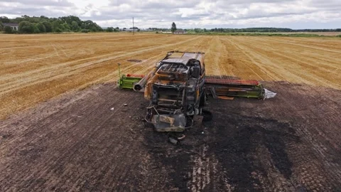 Drone Orbit Shows Burnt Combine Sitting On Scorched Field Patch Under Cloudy Sky Stock Footage 323277201