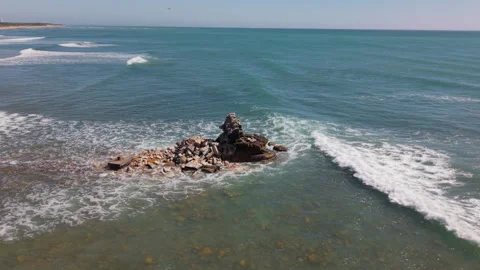 Drone Orbiting Close to Crumbled Beacon in Shallow Sea with Waves Crashing Again Stock Footage 306317452
