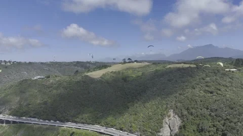 Drone orbits to the left around group of paragliders hovering over coast Stock Footage 326702438