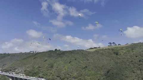 Drone orbits to the left below a sky full of paragliders on a sunny day Stock Footage 326765761