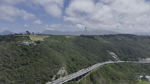 Drone orbits to the left over coastal highway as paragliders fill the sky Stock Footage 326702272
