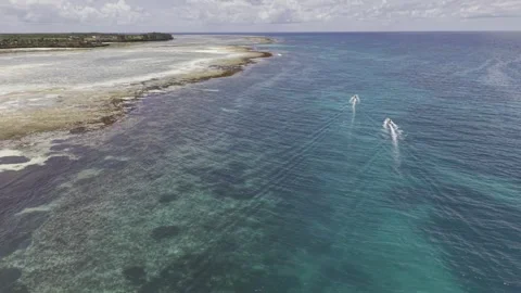 Drone orbits over sea after tide pools at low tide while speed boats pass by Stock-Footage 346158541