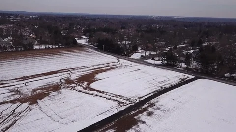 Drone over snow covered field moving toward road and houses Stock Footage 104316935