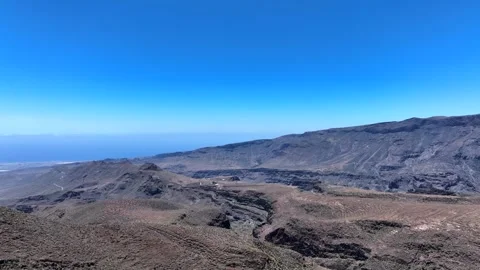 Drone over volcanic mountains with distant coastline and blue ocean and sky Stock Footage 310683145
