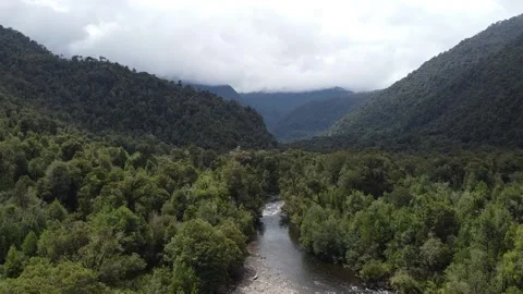 Drone pan of rolling forest mountains between clouds in Chile and a river Vidéo 136212975