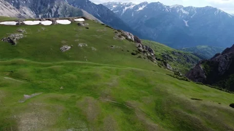 Drone panning shot showcasing rolling green hillsides with snow patches opening Stock Footage 337138731