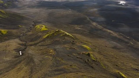 Drone perspective of dark volcanic terrain with yellow-green moss-covered con Stock Photos