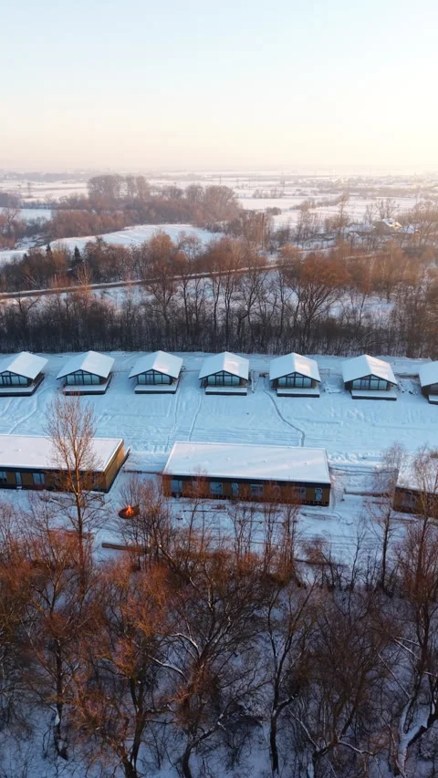 Drone perspective of timber framed homes in snowy landscape at golden hour Stock Footage 346547111