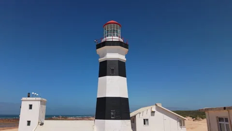 Drone Pull-Away from Lighthouse Revealing Ocean, Beach, Sand, Blue Sky, and Gree Stock Footage 306255091