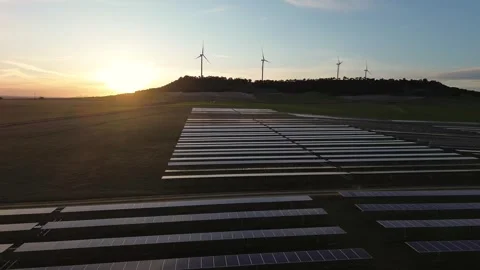 Drone Pull Back Over Solar Farm at Sunset with Wind Turbines Stock Footage 330051272