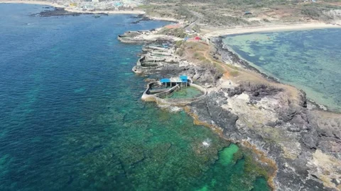 Drone pull back revealing coastal aquaculture facility and rocky cape 4K Stock Footage 336230449