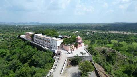 Drone pull-out from hilltop temple revealing village and greenery Video stock 310488226