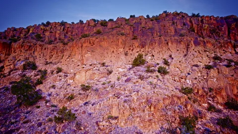 Drone pullback from red rock outcrop exposing a glowing cliff face bathed in Video stock 334070864