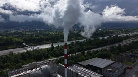 Drone pulling back from industrial chimney with smoke under storm clouds Stock Footage 335038396