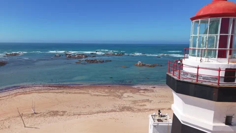 Drone Pulling Back from Ocean and Rocks to Reveal Lighthouse, Road, and People W Stock Footage 306292919