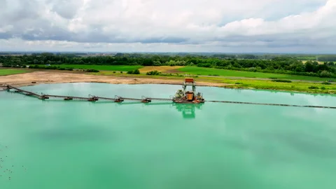 Drone pulling back over turquoise lake with industrial construction site Stock Footage 315551874