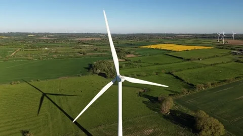 Drone pulling back from rotating wind turbine over green countryside fields Stock Footage 333935897