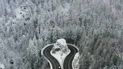 Drone pulling back from winding mountain road around rock revealing snowy forest Video stock 331986624
