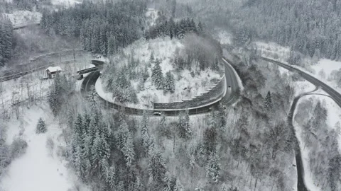 Drone pulling back from winding mountain road hairpin with cars revealing snowy  Stock-Footage 332003555