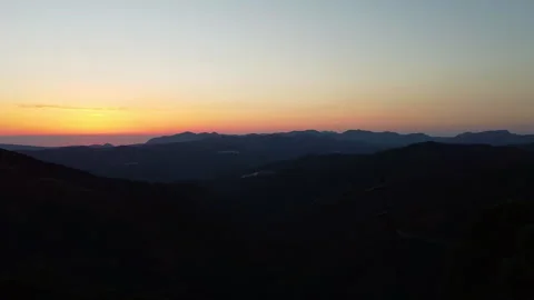 A drone pulls back of the sun setting over the horizon of mountain ranges Stock Footage 244900621