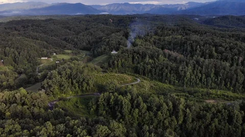Drone Push in Towards Tower of Smoke coming from woods with small curving roads. Stock Footage