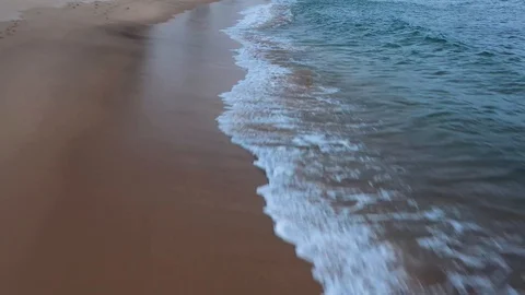 Drone racing along a beach looking down at the waves rolling in Видео 124879353