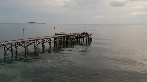 Drone, Raja Ampat orbiting around a wooden jetty at sunset with islands Stock Footage 130314822