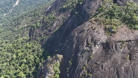 Drone retreating above giant rock with resilient trees on rugged mountain 動画素材 336956374