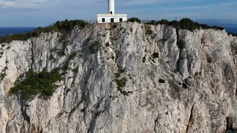 Drone rising above coastal cliffs to reveal a lighthouse, blue sea, rocky 스톡 동영상 336985451
