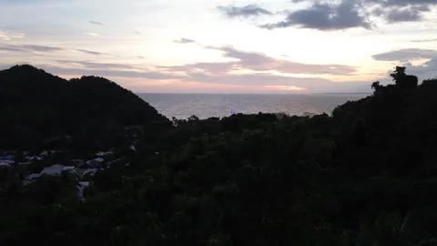 Drone rising above forested mountain revealing sunset Apo Island Philippines Video stock 332615565