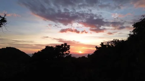 Drone rising above forested mountain revealing sunset Apo Island Philippines Video stock 332615587
