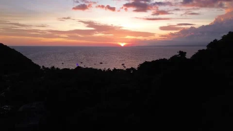 Drone rising above forested mountain revealing sunset Apo Island Philippines Video stock 332615717