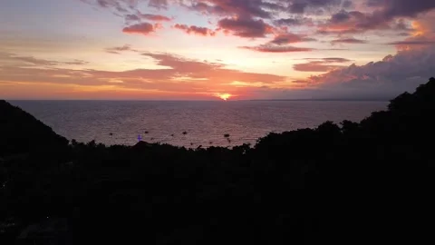 Drone rising above forested mountain revealing sunset Apo Island Philippines Video stock 332615719