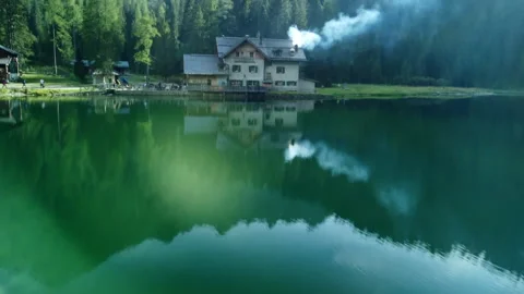 Drone rising from lake surface to lakeside cottage with tourists nearby Stock Footage 314197943