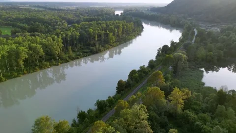 Drone rising next to river Inn, rails and street and lakes with a hill Stock Footage 248702832