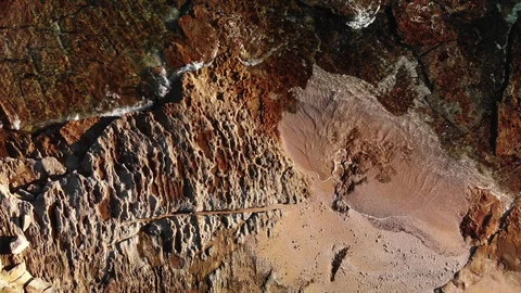 Drone rising over rocks as waves lap against them at Sunrise/sunset Stock Footage 99324227