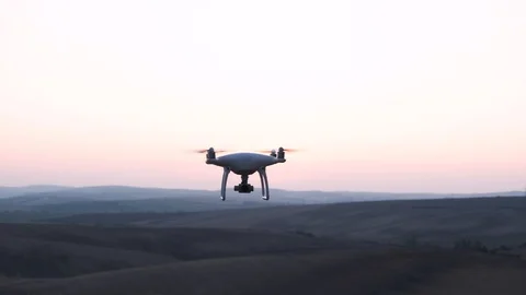 Drone With Rotating Propellers Hanging In The Air. Sunset Scenery In Background Stock Footage 116672491