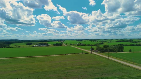 Drone shoot of vast green farmland under a blue sky with large white cumulus Stockbeeldmateriaal 346802420