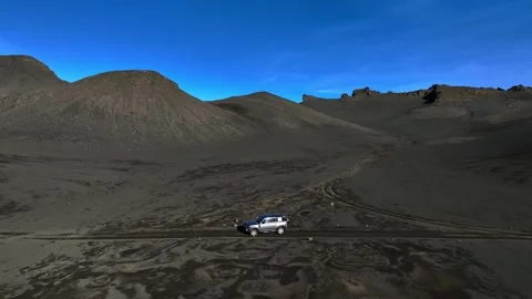 Drone shot of a 4x4 starting to drive from a stop on a barren black volcanic Stock Footage 332130960